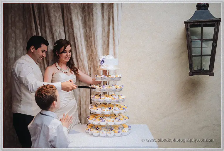 Amanda and Craig slice the top tier as the page boy claps beneath the black wall lantern