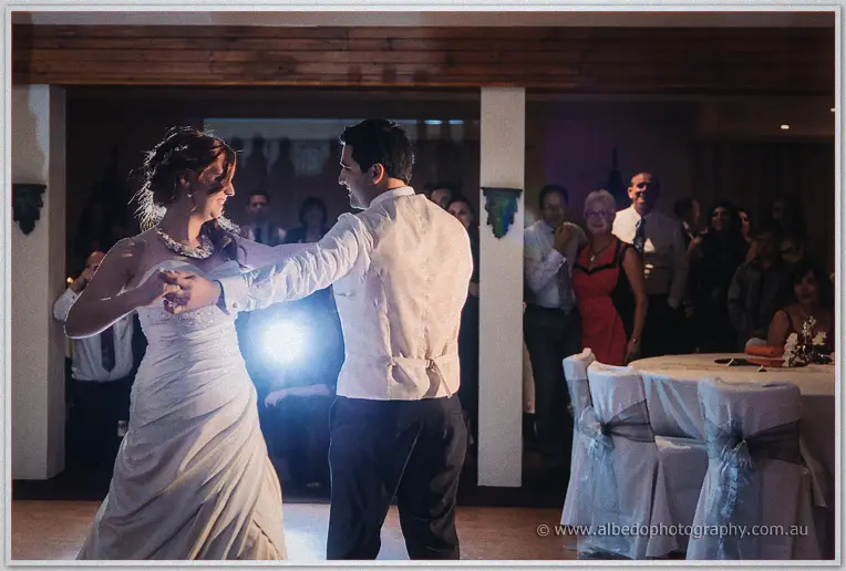 Amanda and Craig sway through their first dance as guests watch from the warmly lit timber hall