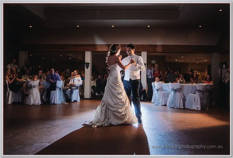 Spotlit newlyweds share their first dance between tables of guests in the reception room at Brookleigh