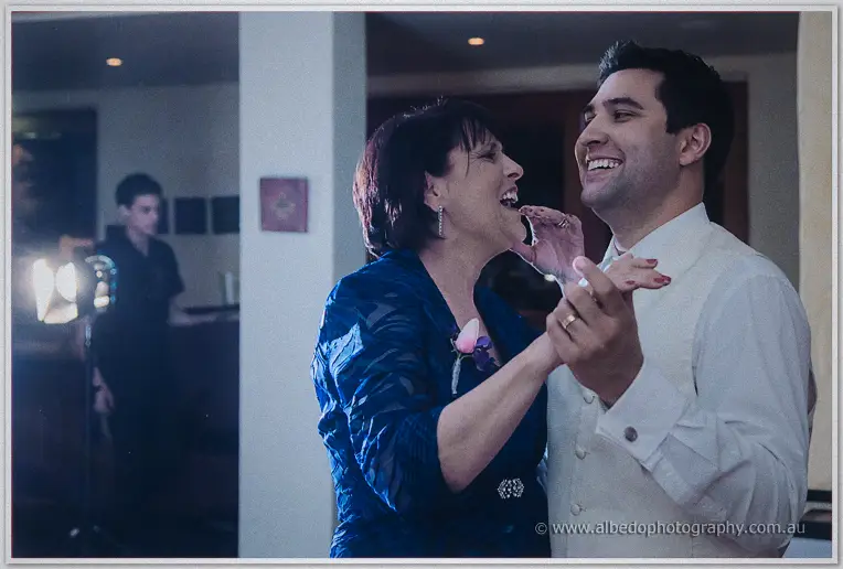 Craig laughs while dancing with his mother in a blue dress inside the warmly lit reception room
