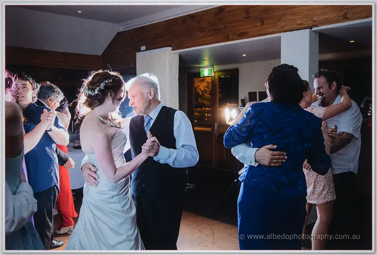 Amanda dances with an older gentleman in a dark vest amid a busy floor of dancing reception guests