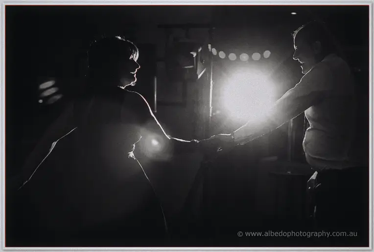Black and white silhouette of two guests laughing as they dance against a bright doorway glow