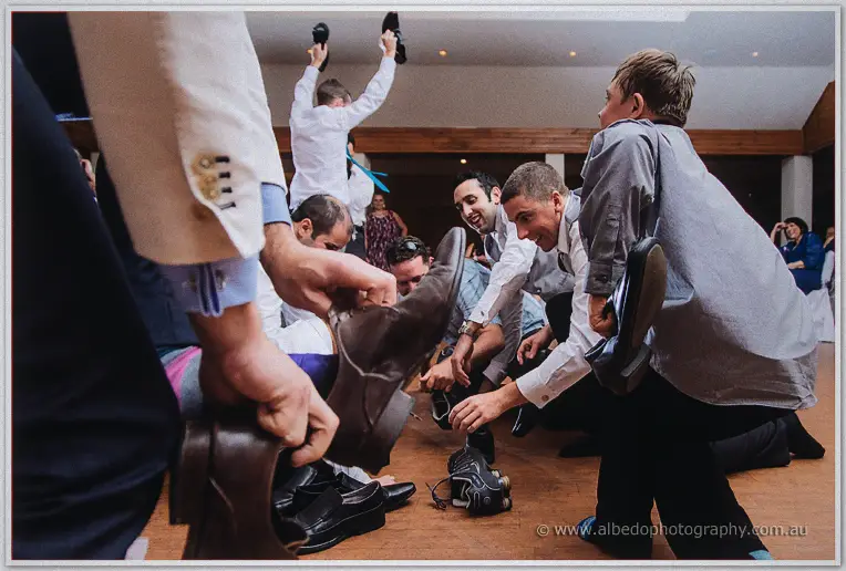 Groomsmen and boys tug shoes from a heap on the dance floor for a traditional shoe game