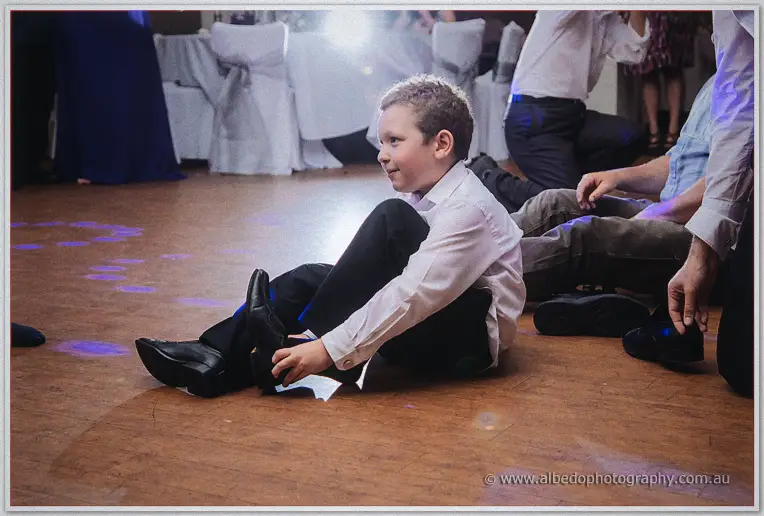 Page boy sits on the dance floor working a dress shoe onto his foot during the shoe game