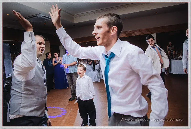 Groomsman in a teal tie high-fives a friend while the page boy watches from the dance floor