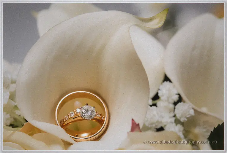 Gold engagement ring and band nestled inside a white calla lily beside baby's breath
