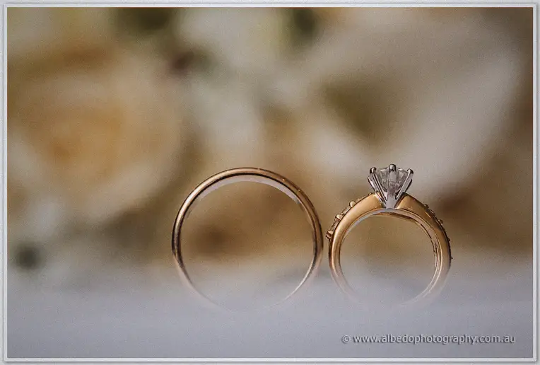 Macro of gold wedding bands and a solitaire diamond ring against blurred cream roses