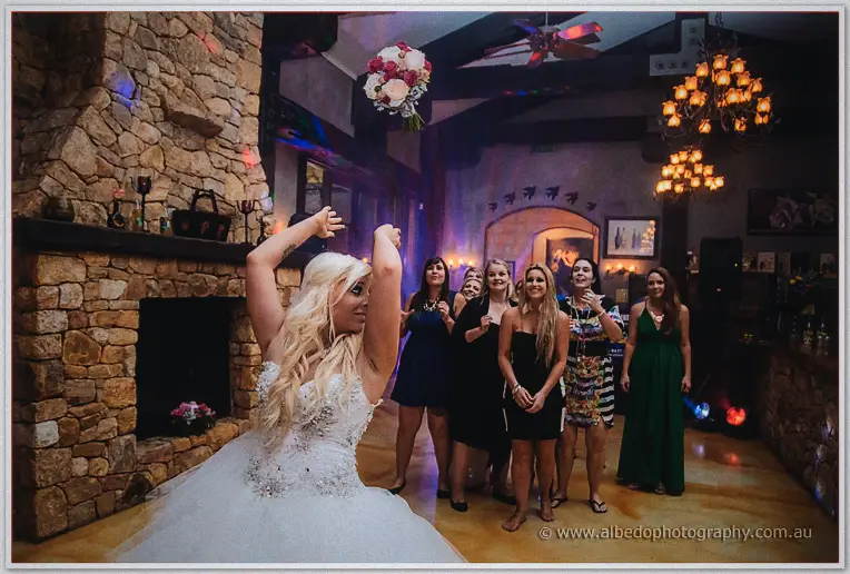 Steph tossing her bouquet over her shoulder to waiting guests by the stone fireplace