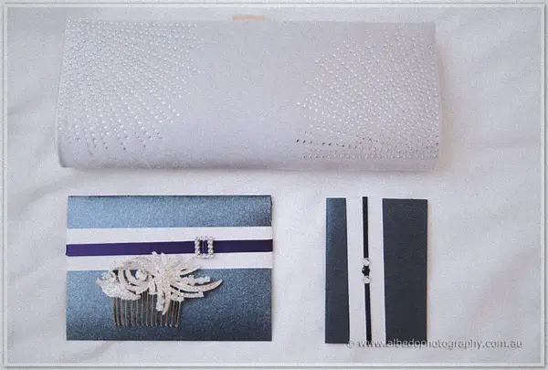A beaded white clutch, navy invitations and a crystal hair comb are laid out on white linen