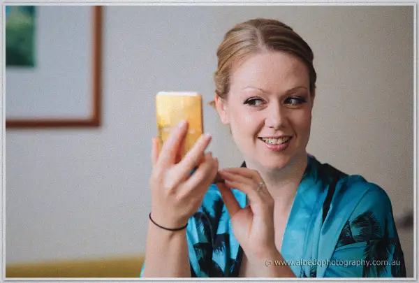 Bride Cayla smiles at her reflection in a hand mirror while wearing a turquoise robe