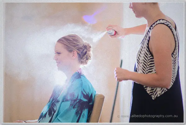 A stylist sprays Cayla's finished updo in a bright room filled with backlit haze