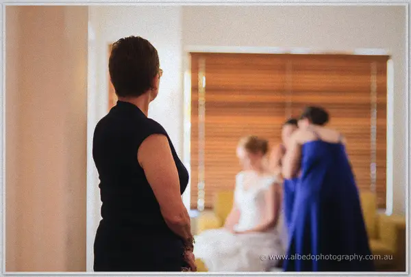 Cayla's mother watches her daughter while bridesmaids in blue dresses soften-focus in the background