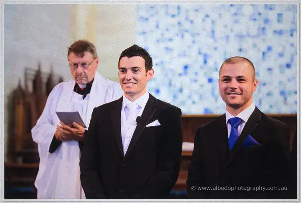 Groom Joe beams beside his best man and the robed celebrant at the cathedral altar