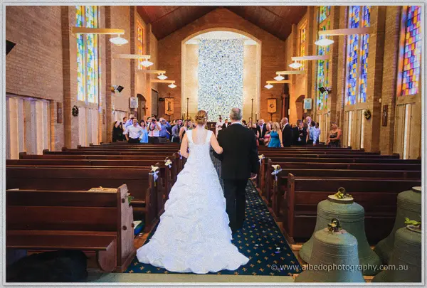 Cayla walks the cathedral aisle on her father's arm past pews of standing guests
