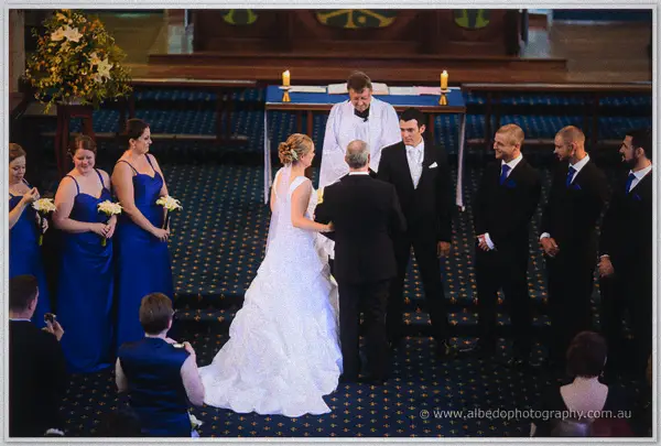Cayla's father hands her to Joe before the priest with the bridal party gathered around