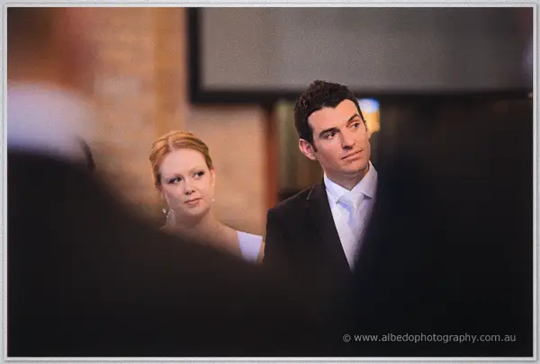 Cayla and Joe glance toward guests from the altar in warm window light