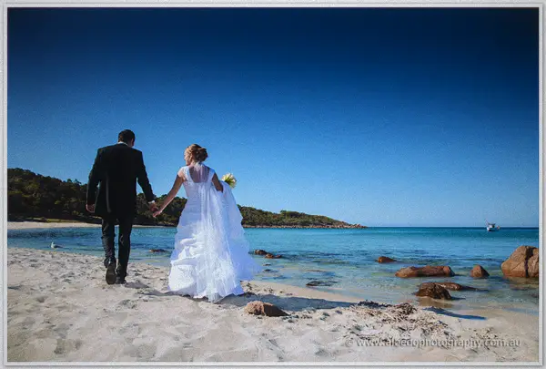 The couple strolls hand in hand along the empty white beach toward turquoise water