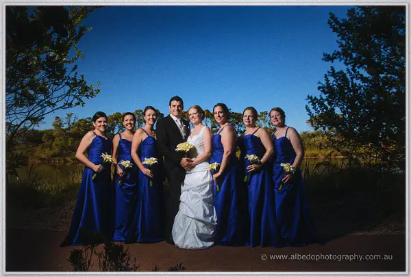 Cayla and Joe flanked by seven bridesmaids in royal blue before a dusky wetland sunset