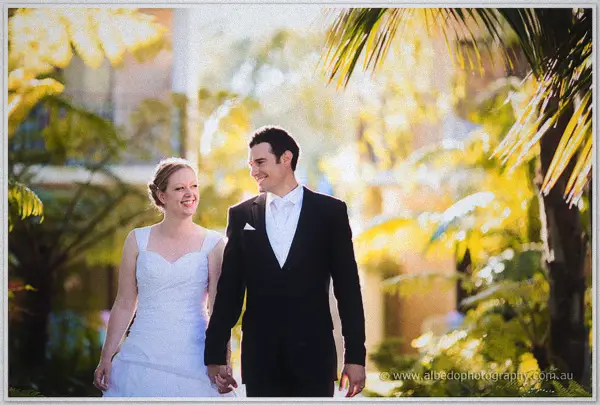 The newlyweds walk hand in hand through the sunlit tropical grounds laughing