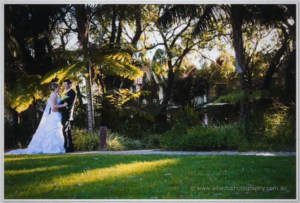 Wide garden scene of the couple embracing on a sunlit lawn beside resort chalets