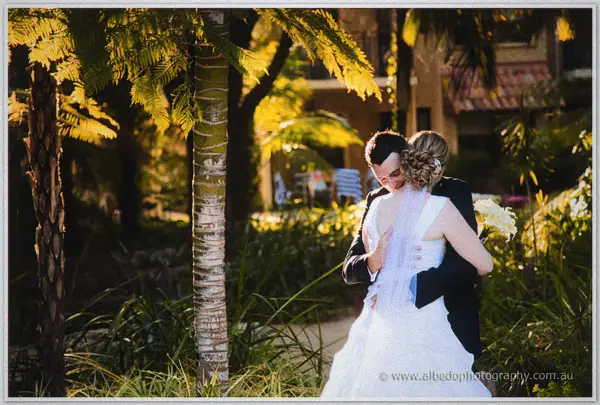 Joe wraps Cayla in a hug beside tree ferns, her veil catching the last light