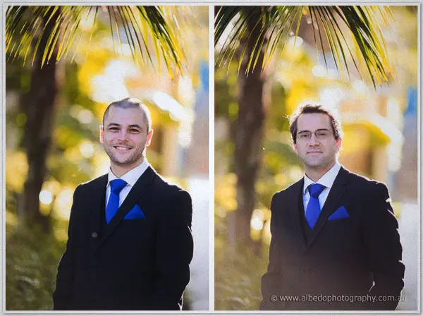 Two groomsmen in matching suits and blue ties stand among backlit palms in the golden Wyndham Resort gardens