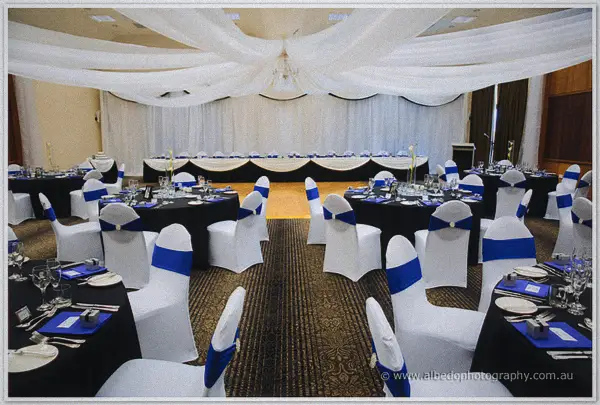 White draping and a chandelier crown the Wyndham Resort ballroom where the bridal table waits with blue sashes