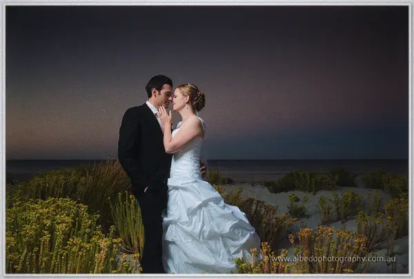 Cayla and Joe kiss among flowering coastal bushes as deep purple twilight settles over the sea at Dunsborough
