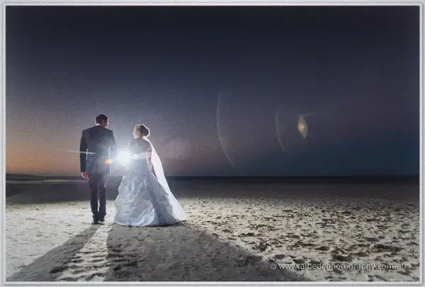 Hand in hand, the couple walks away down the darkening beach, backlit between long shadows on the sand