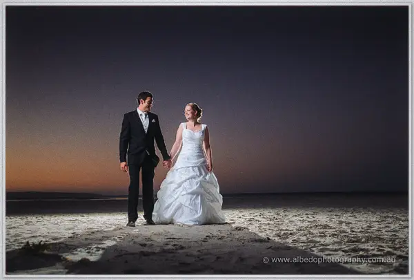 Full length on the empty dusk beach, Cayla and Joe hold hands against the last warm light on the horizon