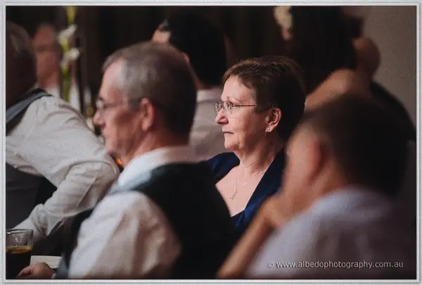 A guest in navy listens intently among softly blurred faces at the candlelit reception tables
