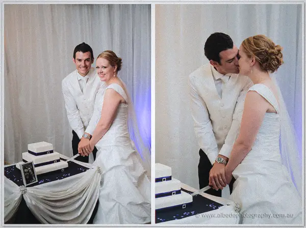 Cayla and Joe cut their navy-ribboned tiered cake, Joe kissing her temple as the blade pauses mid-slice