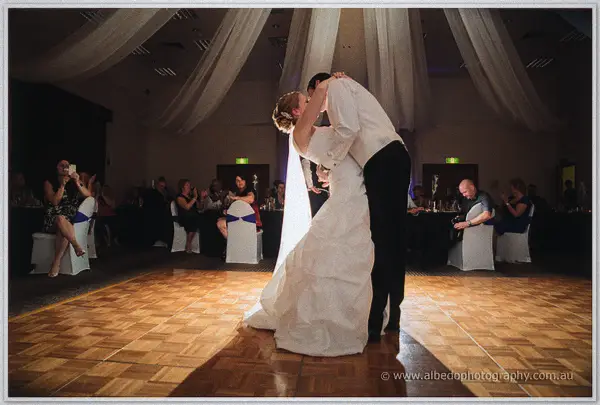Joe dips Cayla into a kiss on the parquet dance floor as guests watch and film beneath the draped ceiling