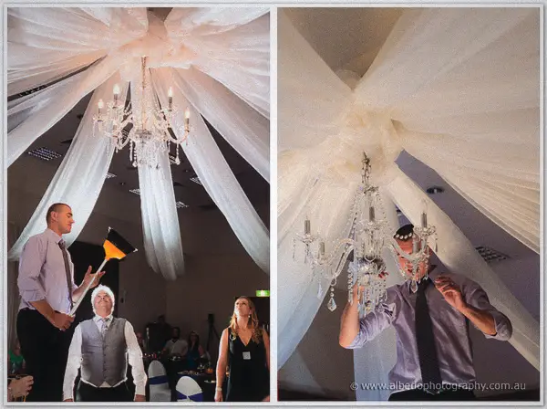 Staff in shirts and ties steady and light a crystal chandelier on a long pole beneath the draped ceiling
