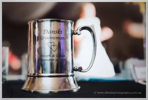 An engraved silver tankard rests on the table while the couple dances as soft bokeh behind it