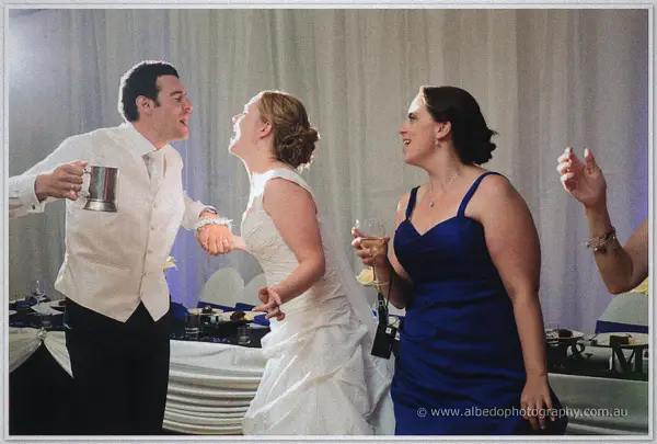 Joe sings with his tankard raised alongside the laughing bride and a bridesmaid in blue mid dance