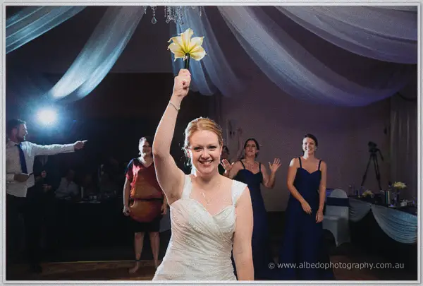 Beaming Cayla raises her yellow calla lily high after the bouquet toss as bridesmaids reach behind her