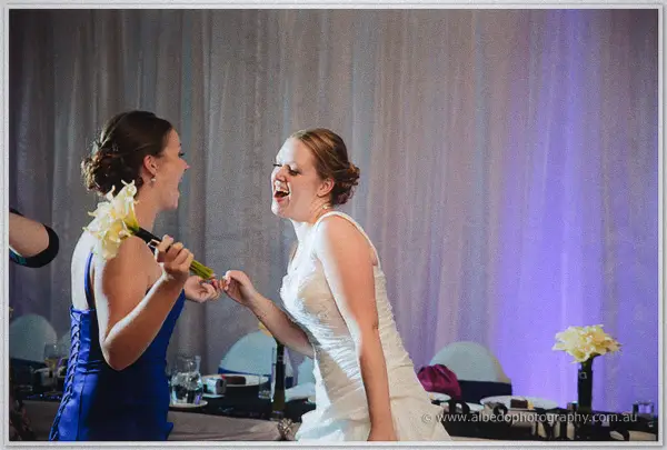 Cayla laughs joyfully as the winning bridesmaid in blue holds up the yellow calla bouquet beside her