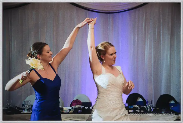 Cayla twirls her bridesmaid under a raised arm on the dance floor, both laughing in the lavender glow