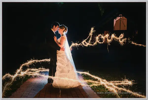 Cayla and Joe embrace on a brick path at night as sparkler light spells love around them at Wyndham Resort