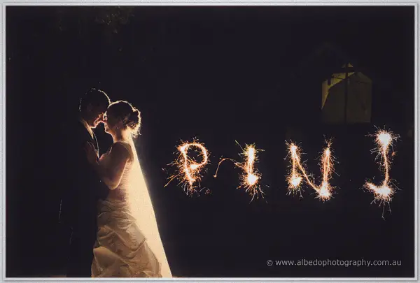 Forehead to forehead in the dark, the couple stands beside sparkler letters spelling P, N and J