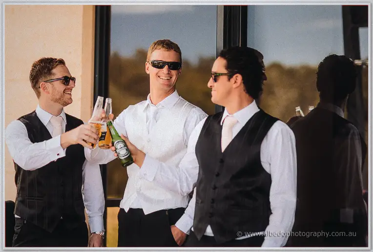 Sunglasses on, the groom and groomsmen clink beer bottles in a sunlit toast outside the winery