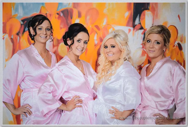 Bride and three bridesmaids in satin robes strike confident poses before a fiery abstract mural