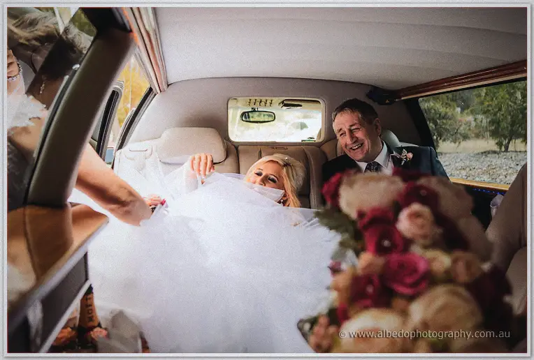 Steph laughs as she arranges her tulle skirt inside the limousine beside a smiling man in a suit.