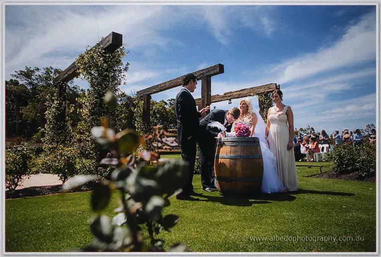 Luke signs the marriage register on a wine barrel beside the celebrant in the rose garden.