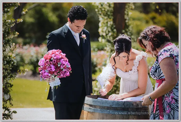 A witness signs the marriage certificate on the wine barrel while the celebrant watches.