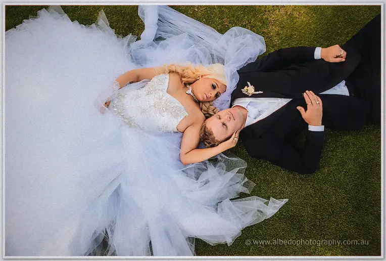 Overhead shot of Steph and Luke lying on the grass, her tulle gown fanned around them.