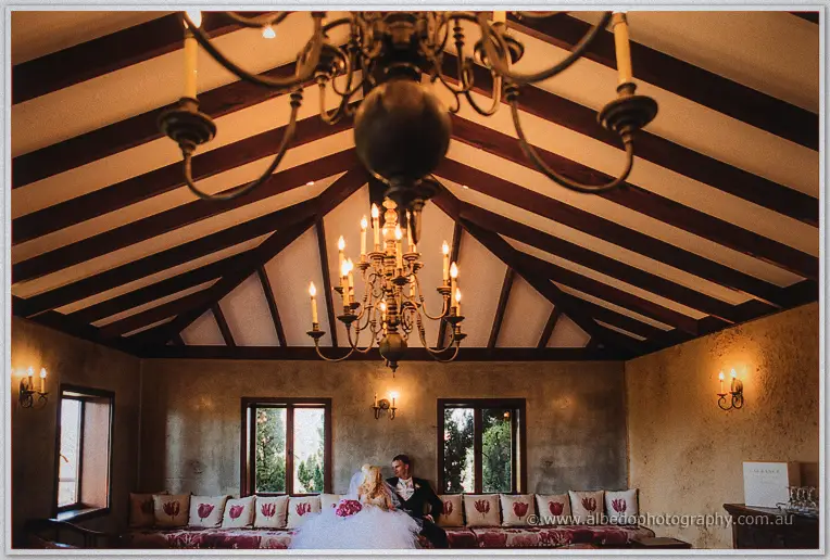 Beneath twin chandeliers, Steph and Luke cuddle on a cushioned window seat.