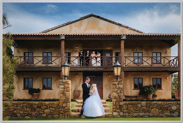 Steph and Luke embrace on the barn steps as the wedding party watches from the balcony above
