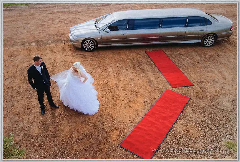 Bride and groom beside their silver limousine on red gravel, red carpet runners laid out nearby